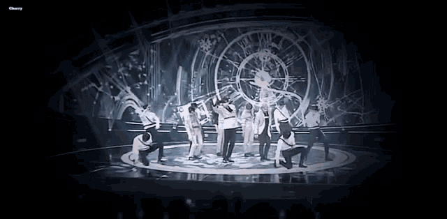 a group of people are dancing on a stage with a clock behind them