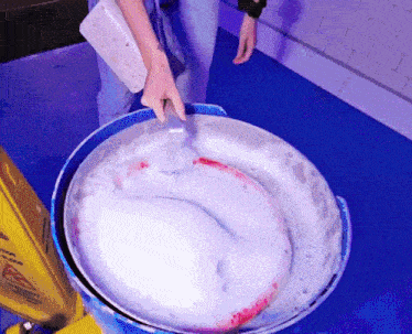 a person is mixing something in a bucket with a yellow caution sign in the background