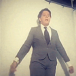 a man in a suit and tie is standing in front of a white wall with his arms outstretched