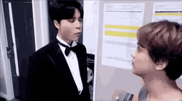 a man in a tuxedo and bow tie is standing next to another man in a room .