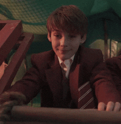 a young boy in a suit and tie holds onto a rope