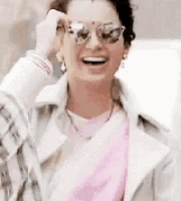a woman wearing sunglasses and a pink scarf is smiling and laughing .