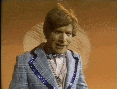 a man in a blue plaid suit and bow tie is standing in front of a clock .
