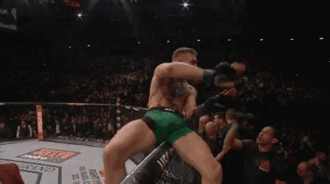 a man is kicking another man in the face while standing in a boxing ring in front of a crowd .