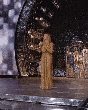 a woman in a gold dress sings into a microphone