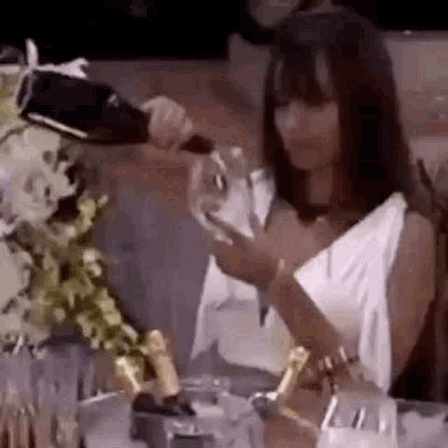 a woman in a white dress is pouring champagne into a glass .