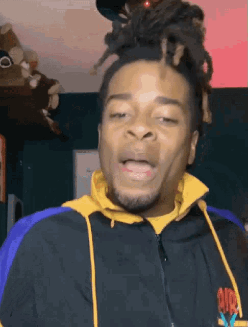 a man with dreadlocks is wearing a black and yellow jacket with the word old on the sleeve