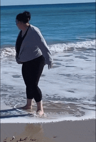 a woman walking barefoot on the beach near the ocean