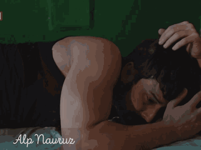 a man laying on a bed with the name alp nawruz written on the bottom right