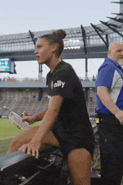 a woman wearing a black shirt that says ally stands in a stadium