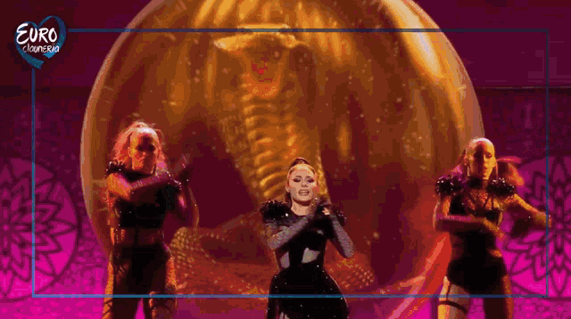 a group of women are dancing on a stage in front of a euro camera banner