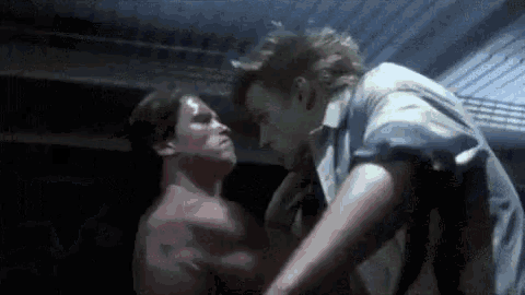 two men are standing next to each other in a dark room and fighting .