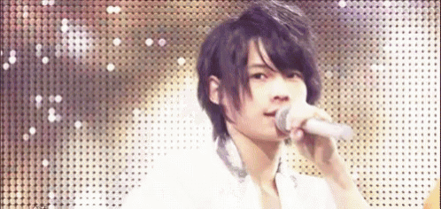 a young man is singing into a microphone on a stage in front of a polka dot wall .