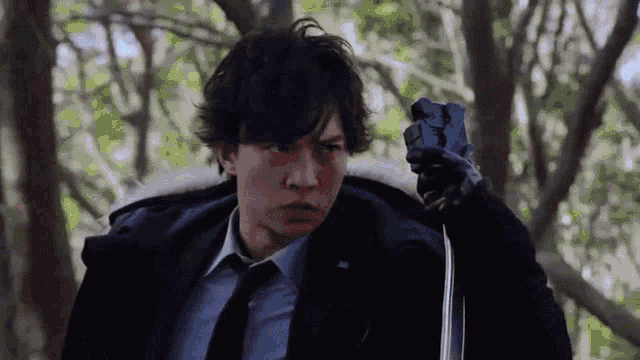 a man in a suit and tie is holding a gun in his hand in the woods .