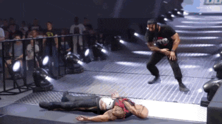 a wrestler is laying on the ground while another wrestler stands in the background