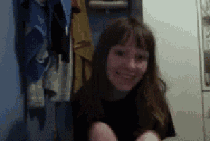 a woman in a black shirt is smiling in a room with clothes hanging on the wall