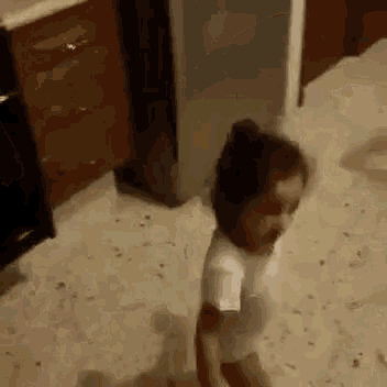 a little girl is sitting on the floor in a kitchen .