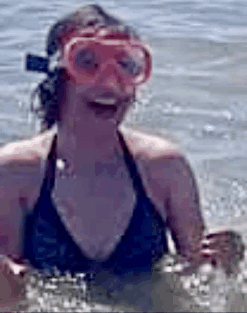 a woman in a bikini is swimming in the ocean wearing a pink mask .