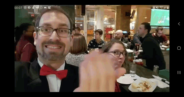 a man wearing glasses and a red bow tie is giving a thumbs up at a restaurant
