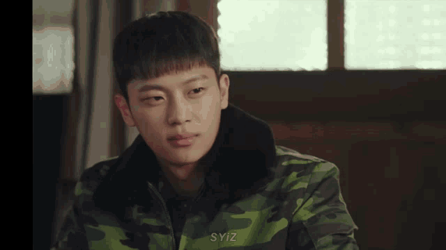 a young man wearing a camouflage jacket with syiz written on the collar