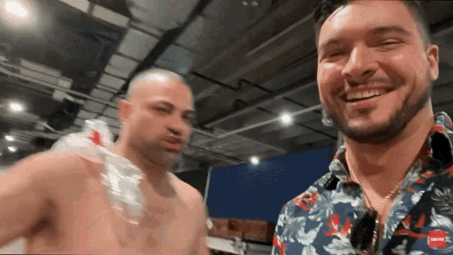 a shirtless man is smiling next to another shirtless man in a floral shirt