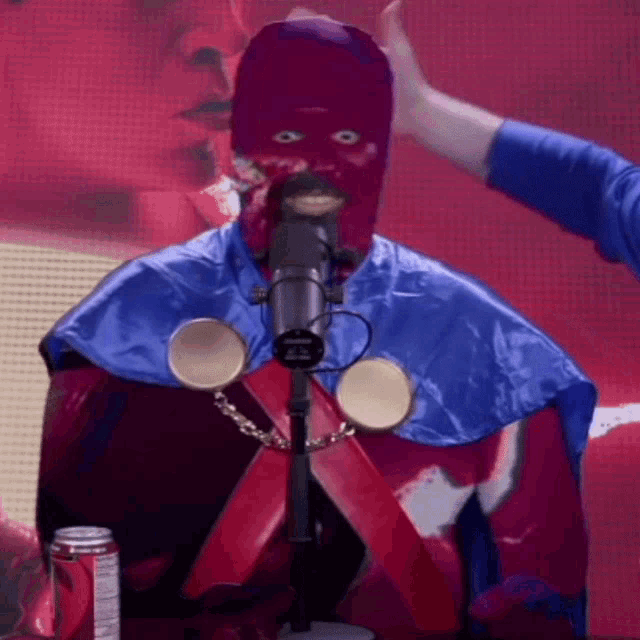 a man in a purple mask is standing in front of a microphone with a can of dr pepper in the background