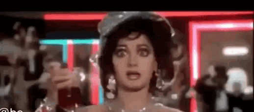 a close up of a woman wearing a hat and earrings in a room with neon lights .