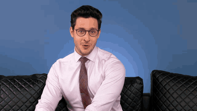 a man wearing glasses and a pink shirt is sitting on a couch