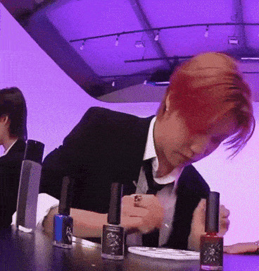 a man in a suit and tie is sitting at a table with bottles of nail polish on it
