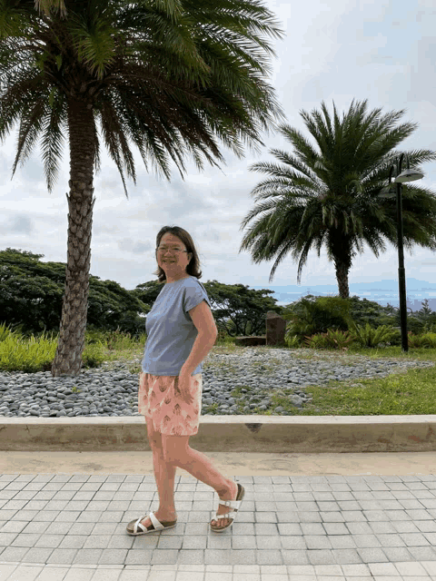 a woman wearing a blue shirt and pink shorts is standing in front of palm trees