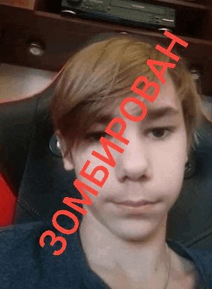 a young man is sitting in a chair and taking a selfie with the words `` zombie '' written on his face .