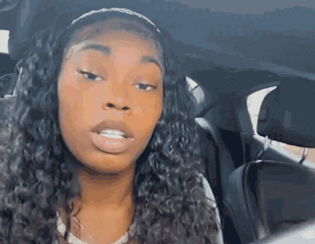 a woman with curly hair is sitting in the back seat of a car with her mouth open .