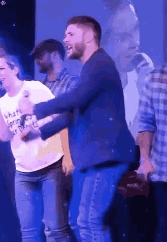a man in a blue jacket is dancing with a woman in a white t-shirt that says what 's spring ?