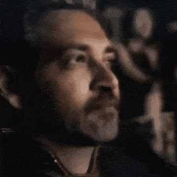 a man with a beard is watching a movie in a dark room .
