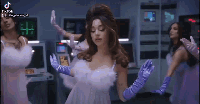 a woman in a white dress and purple gloves is dancing with a group of women in purple dresses .