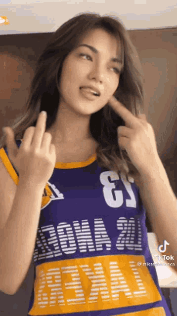 a woman is wearing a purple and yellow basketball jersey and giving the middle finger .
