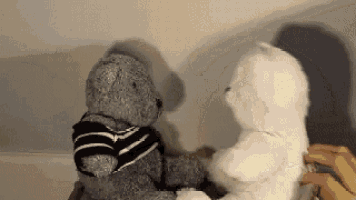 two teddy bears are sitting next to each other and one has a black and white striped shirt on .