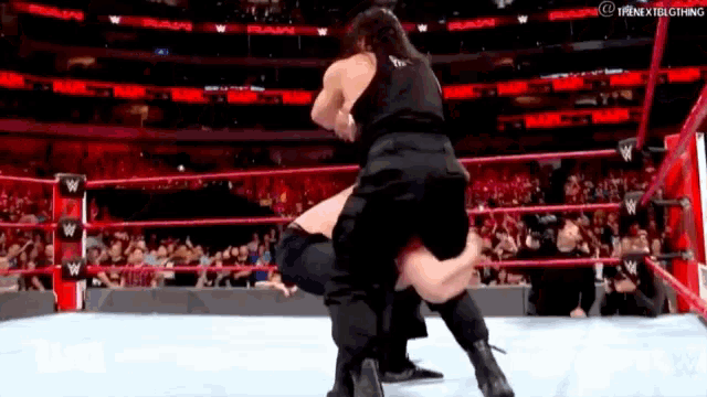 a wrestler is carrying another wrestler on his back in a wrestling ring .
