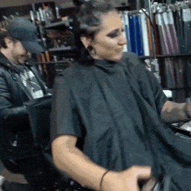 a woman is getting her hair cut by a man wearing a hat that says ny
