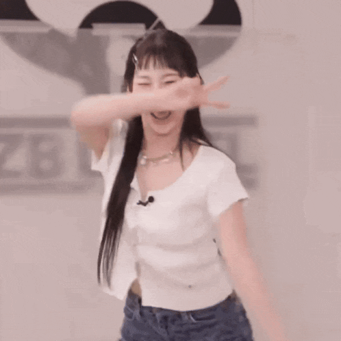 a woman in a white shirt and blue jeans is dancing in an empty room