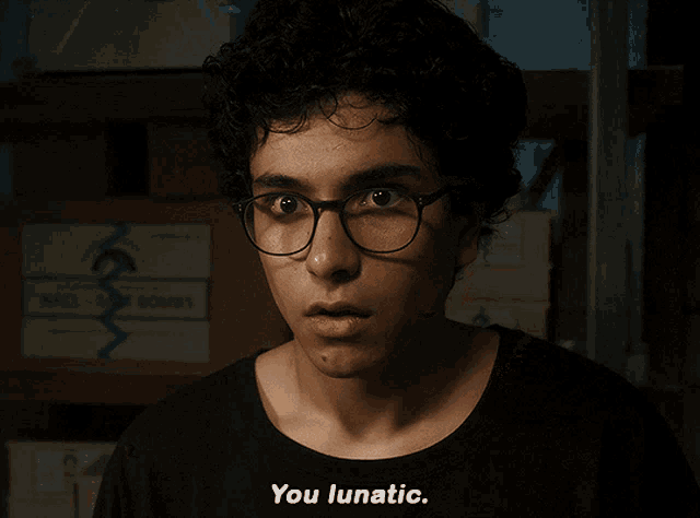 a man wearing glasses says you lunatic in front of some boxes