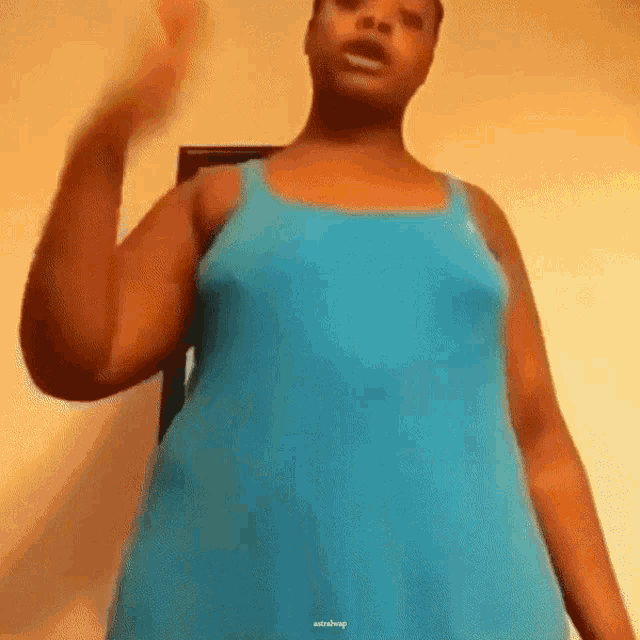 a woman in a blue tank top is standing in front of a yellow wall .