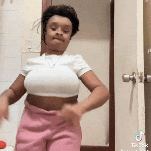 a woman in a white crop top and pink shorts is dancing in a bathroom .