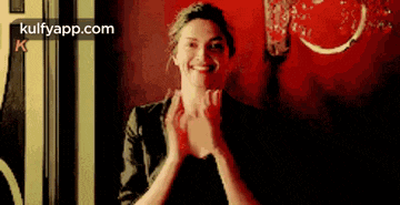 a woman is smiling and clapping her hands in front of a red background .