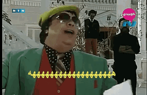 a man wearing a green suit and a yellow hat stands in front of a ntn logo