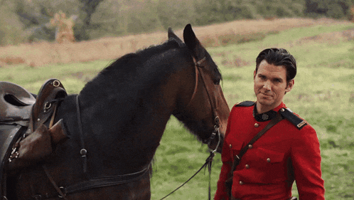 a man in a red uniform stands next to a horse in a field