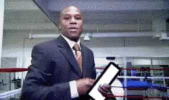 a man in a suit and tie is standing in a boxing ring holding a clipboard