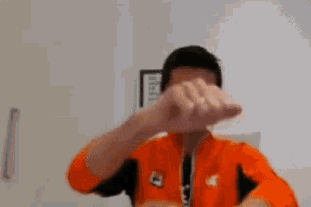 a man in an orange jacket is making a fist with his hands .
