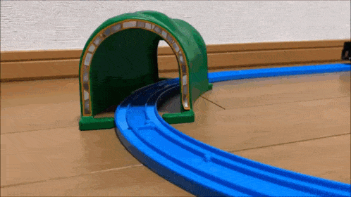 a toy train is going through a green tunnel on a wooden floor