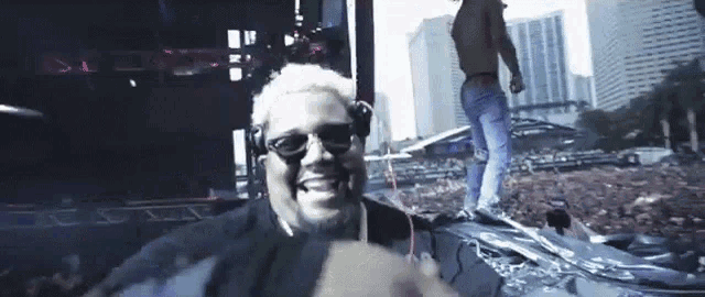 a man wearing headphones and sunglasses is smiling in front of a crowd of people .